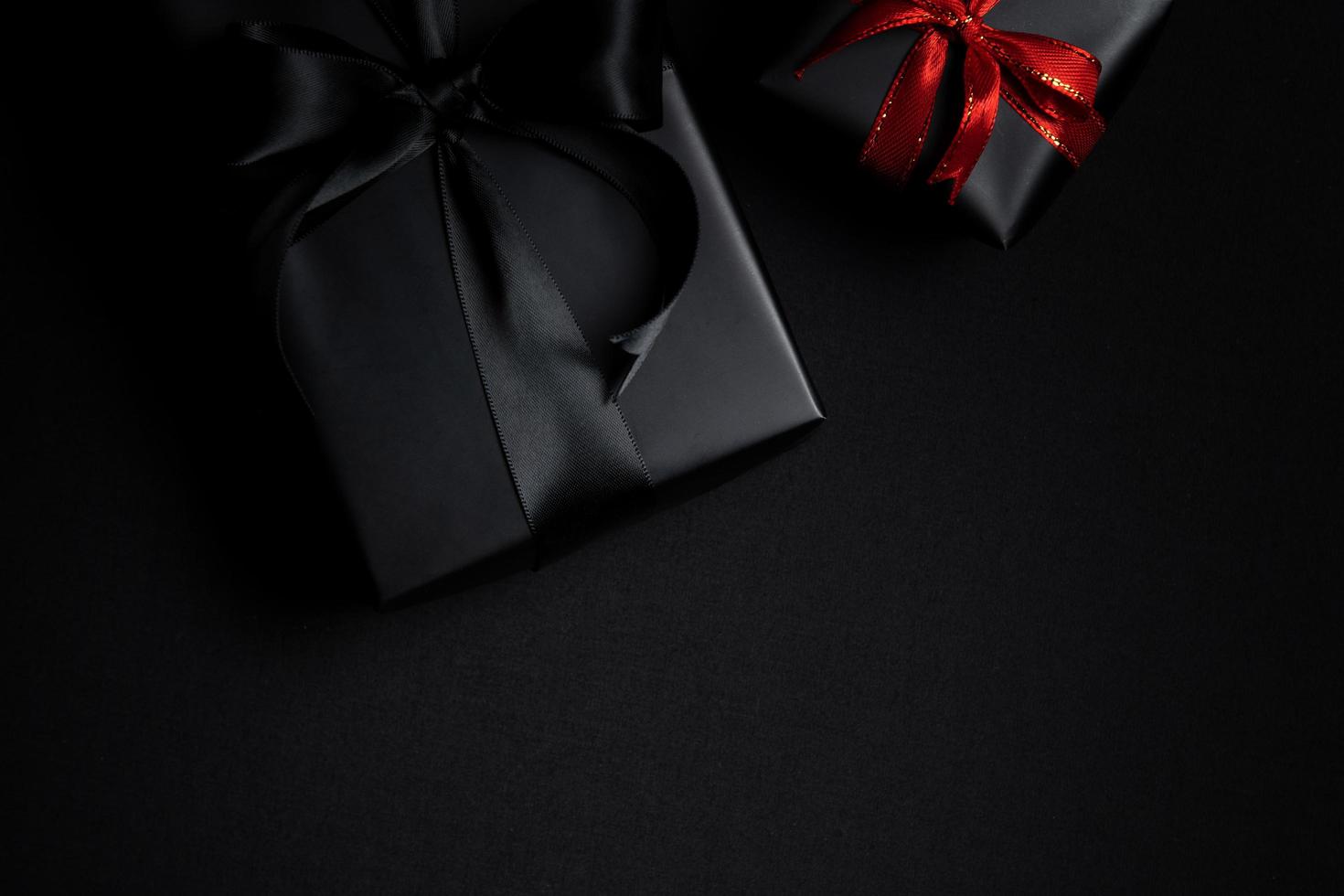 black gift box with red and black ribbons isolated on black background photo