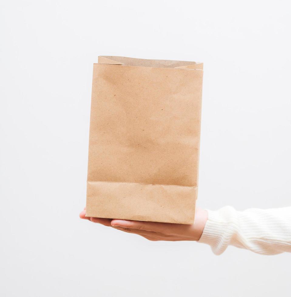 Close up female holds in hand brown clear empty blank craft  eco paper bag on white background. photo