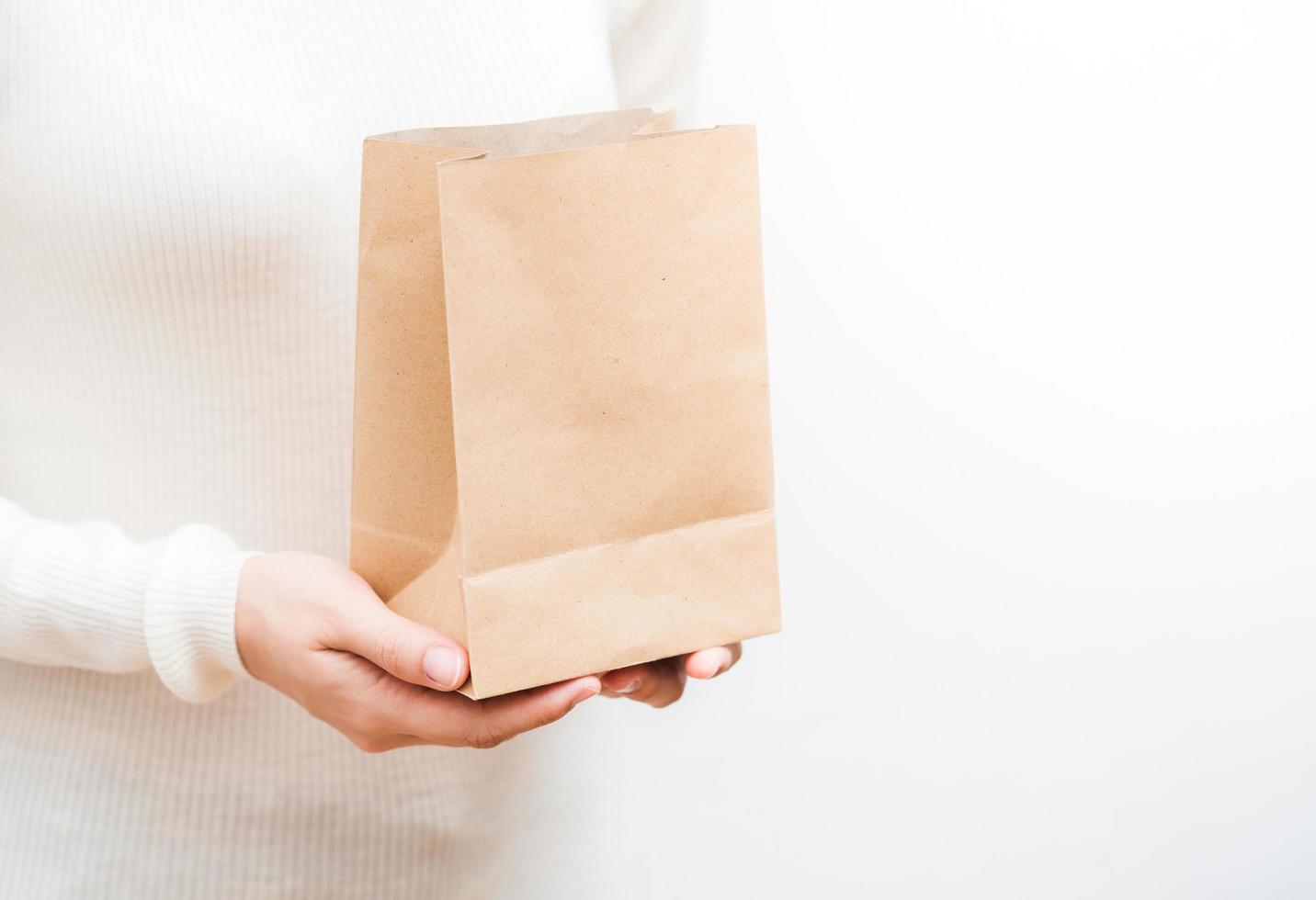 Close up female holds in hand brown clear empty blank craft  eco paper bag on white background. photo
