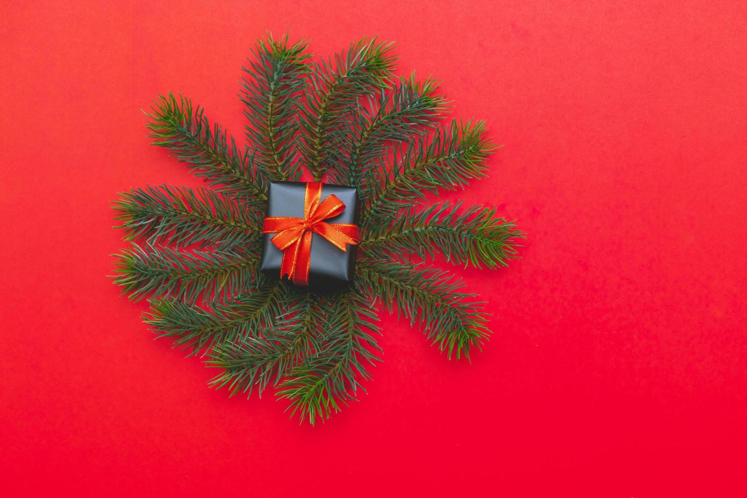 vista superior de la caja de regalo de navidad bolas rojas con ramas de abeto, conos de pino, bayas rojas y campana sobre fondo rojo. foto