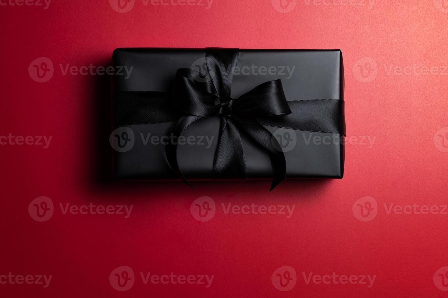 Top view of black gift box with red and black ribbons isolated on red background. photo