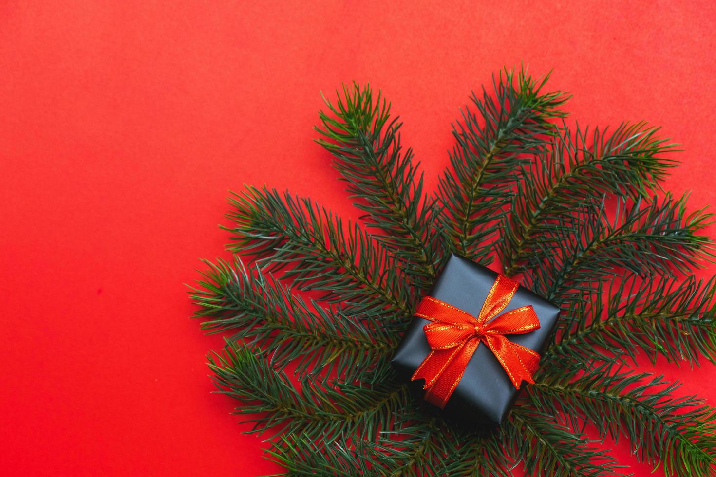 vista superior de la caja de regalo de navidad bolas rojas con ramas de abeto, conos de pino, bayas rojas y campana sobre fondo rojo. foto