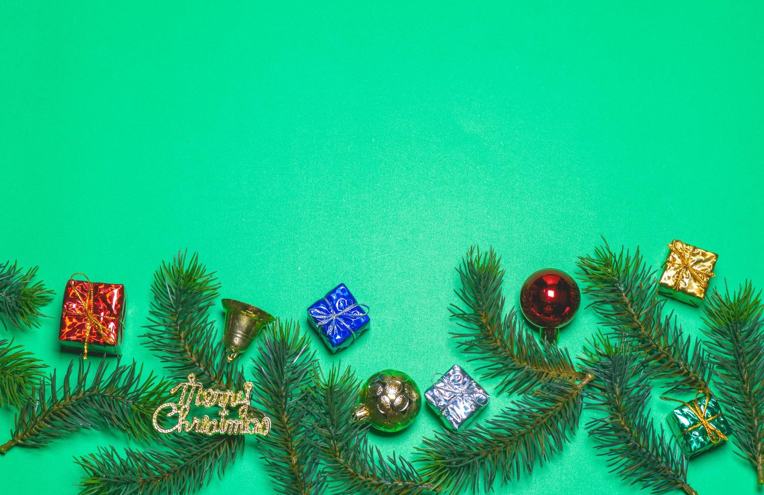 Top view of Christmas gift box red balls with spruce branches and bell on green background. photo