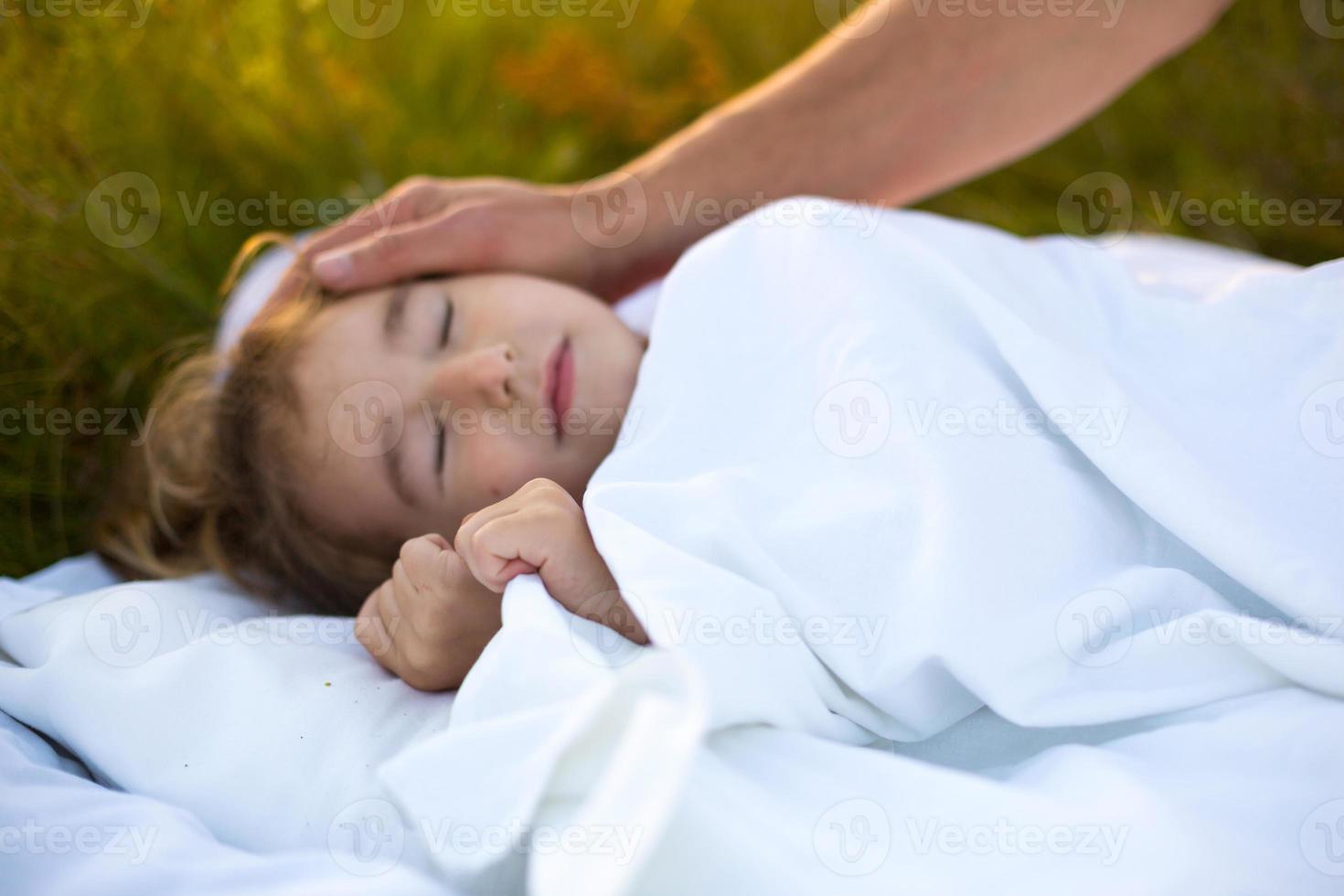 Girl sleeps on white bed in the grass, fresh air. Dad's hand gently pats his head. Care, protection, International Children's Day, mosquito bites photo