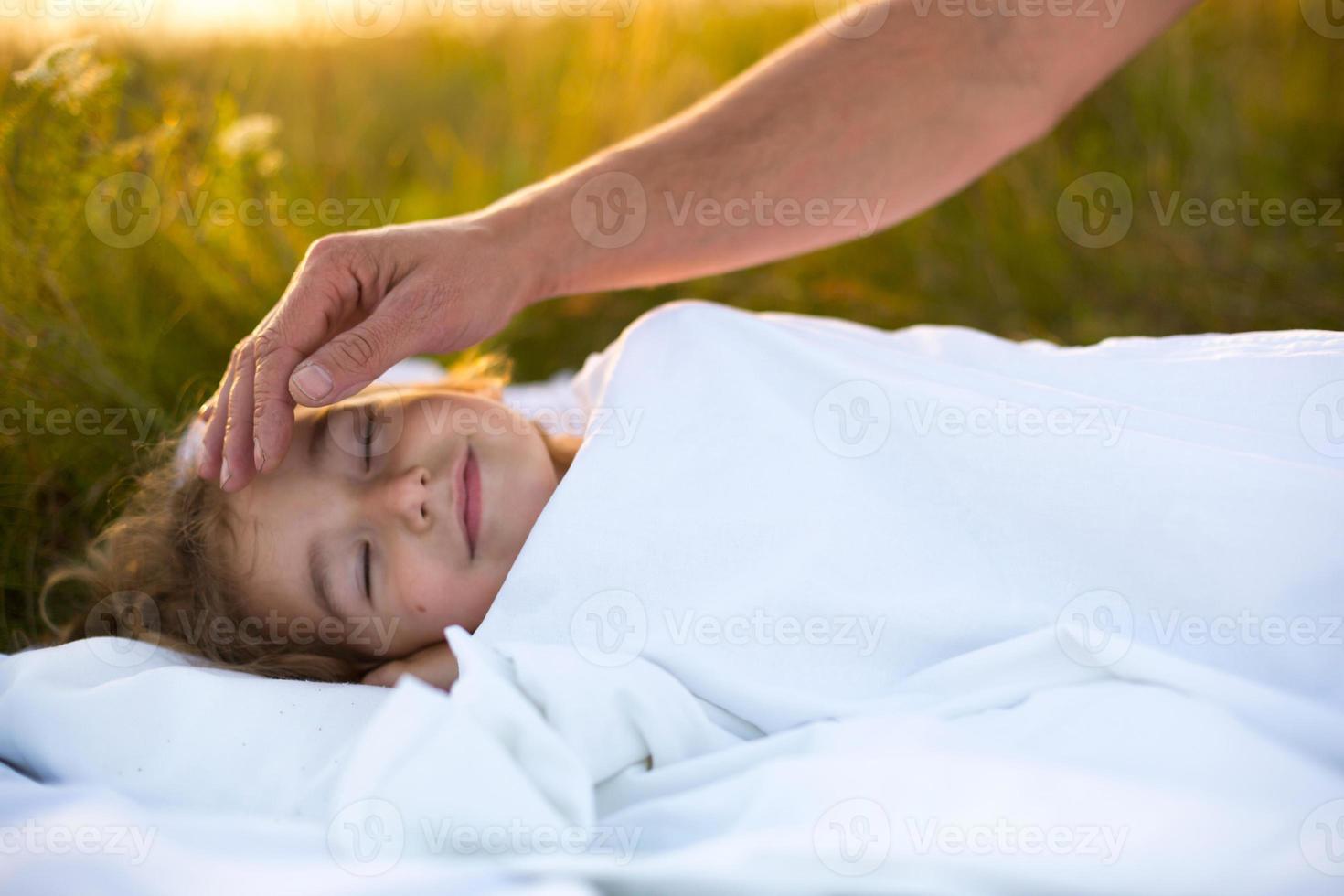 Girl sleeps on white bed in the grass, fresh air. Dad's hand gently pats his head. Care, protection, International Children's Day, mosquito bites photo