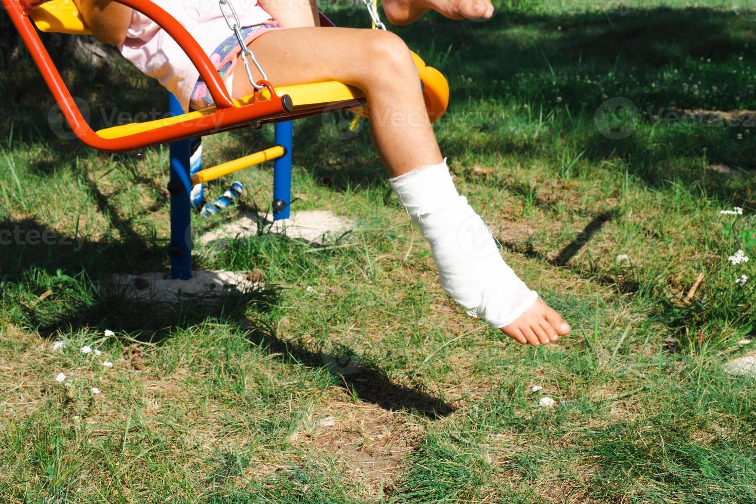 Children's legs are bandaged in plaster - barefoot on a swing. Traumatic equipment, child injury, bruise, sprain, fracture photo