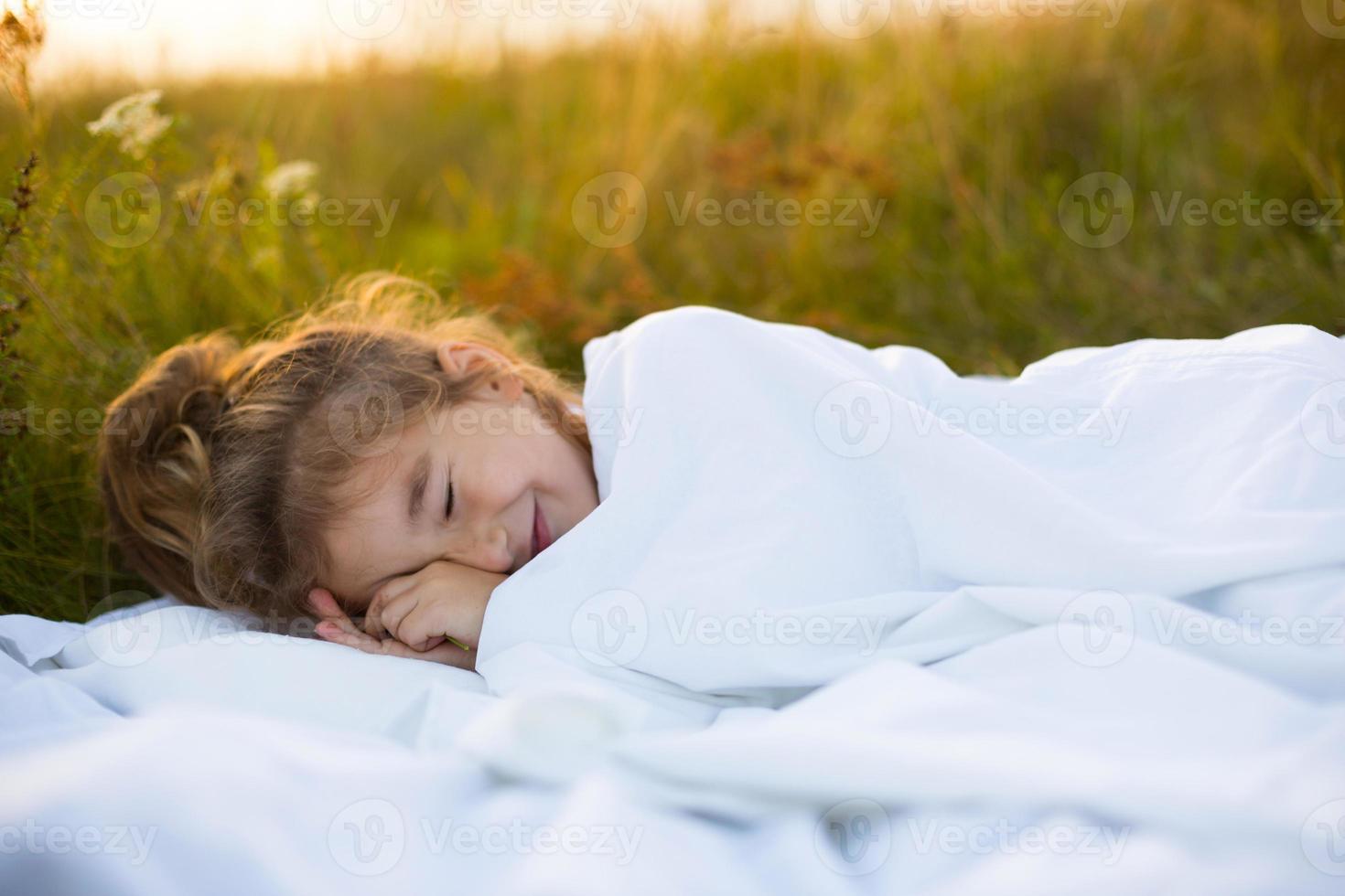 The girl sleeps on white bed linen in nature in the grass, in the fresh air. Protection from mosquitoes, healthy sleep, the benefits of ventilation, hardening, clean nature, ecology, children's health photo