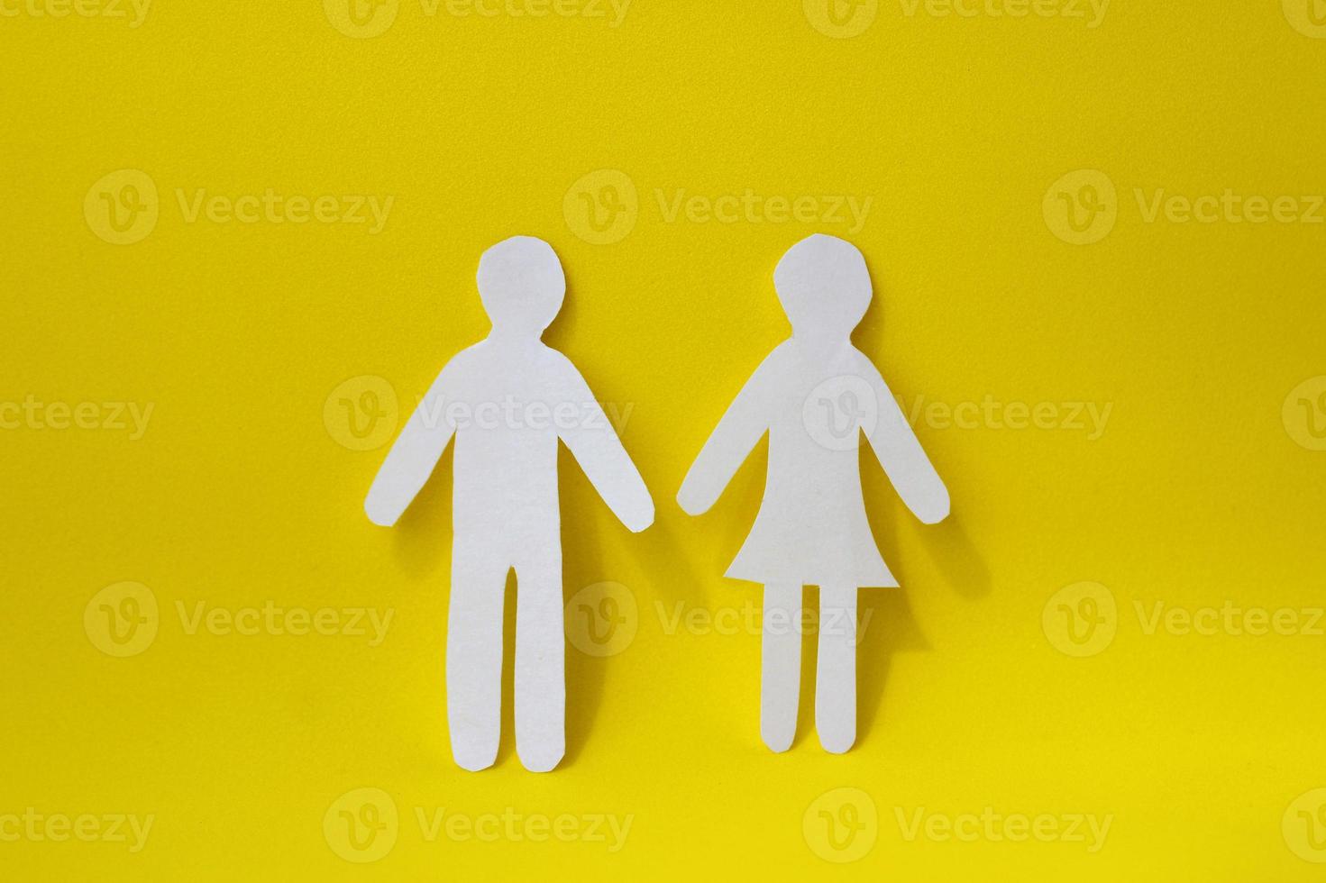 Silhouettes of a man and a woman are carved from white paper, standing side by side on a yellow background. The concept of love, relationships, family photo