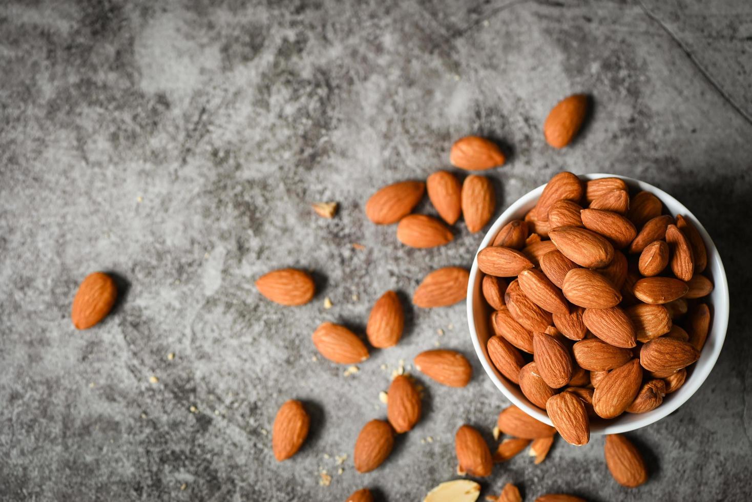 Almonds nuts on white bowl, Delicious sweet almonds on the table dark background, roasted almond nut for healthy food and snack photo