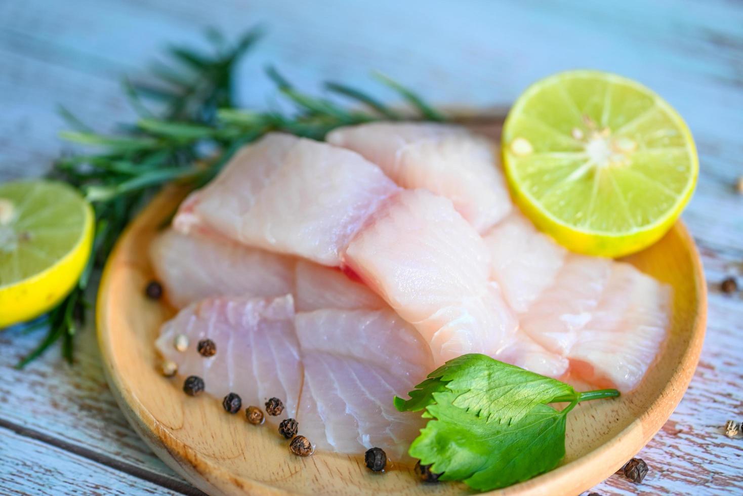 fish fillet on wooden plate with ingredients for cooking, fresh raw pangasius fish fillet with herb and spices black pepper lemon lime and rosemary, meat dolly fish tilapia striped catfish photo