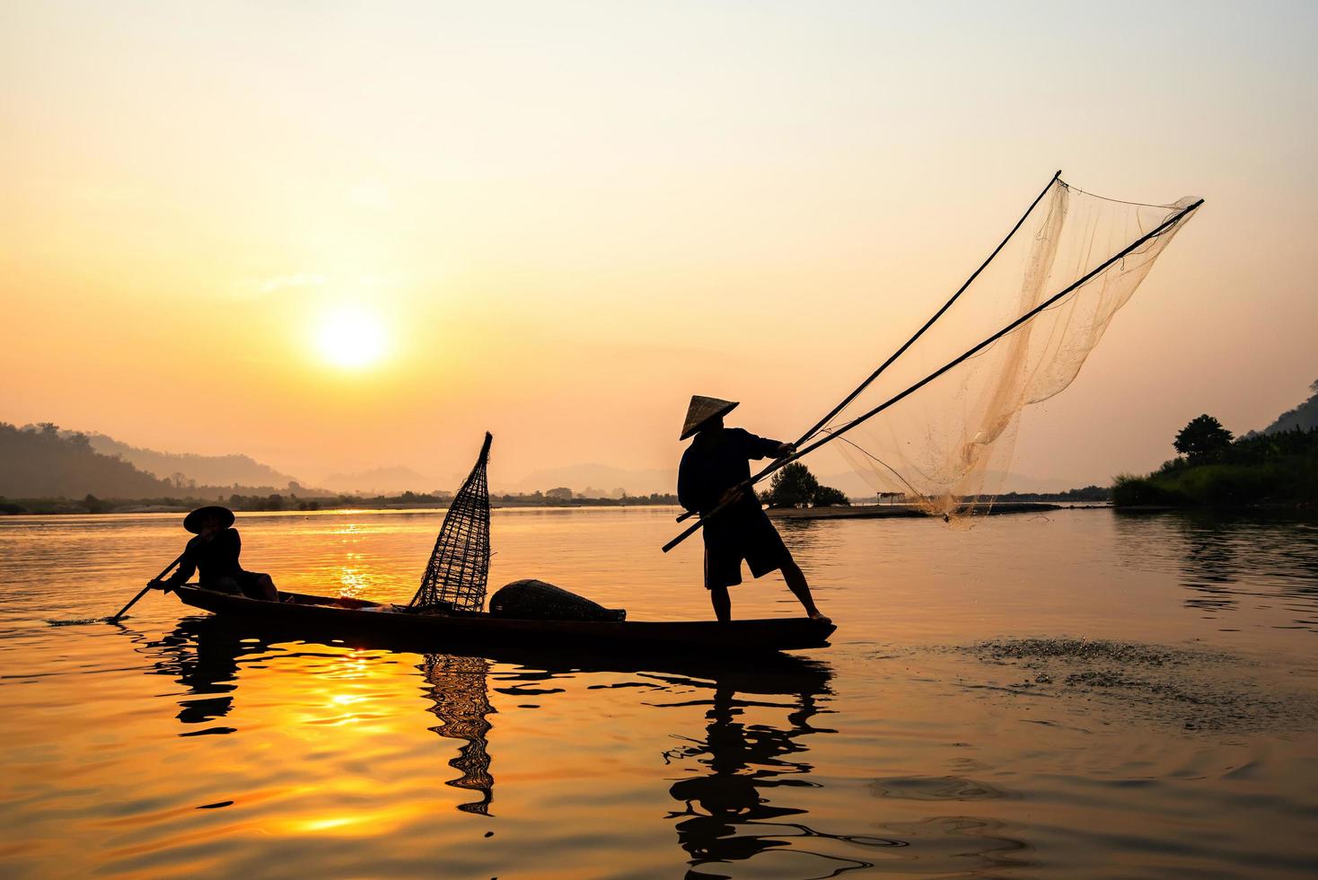 Asia fisherman net using on wooden boat casting net sunset or sunrise in the Mekong river - Silhouette fisherman photo