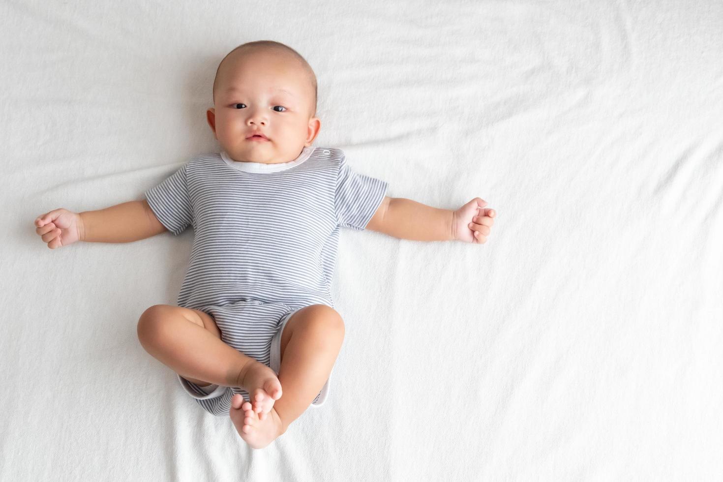 la imagen de la vista superior tiene un área lateral, es un bebé con una camisa a rayas. acuéstese con las piernas en alto y los brazos extendidos sobre la cama. foto