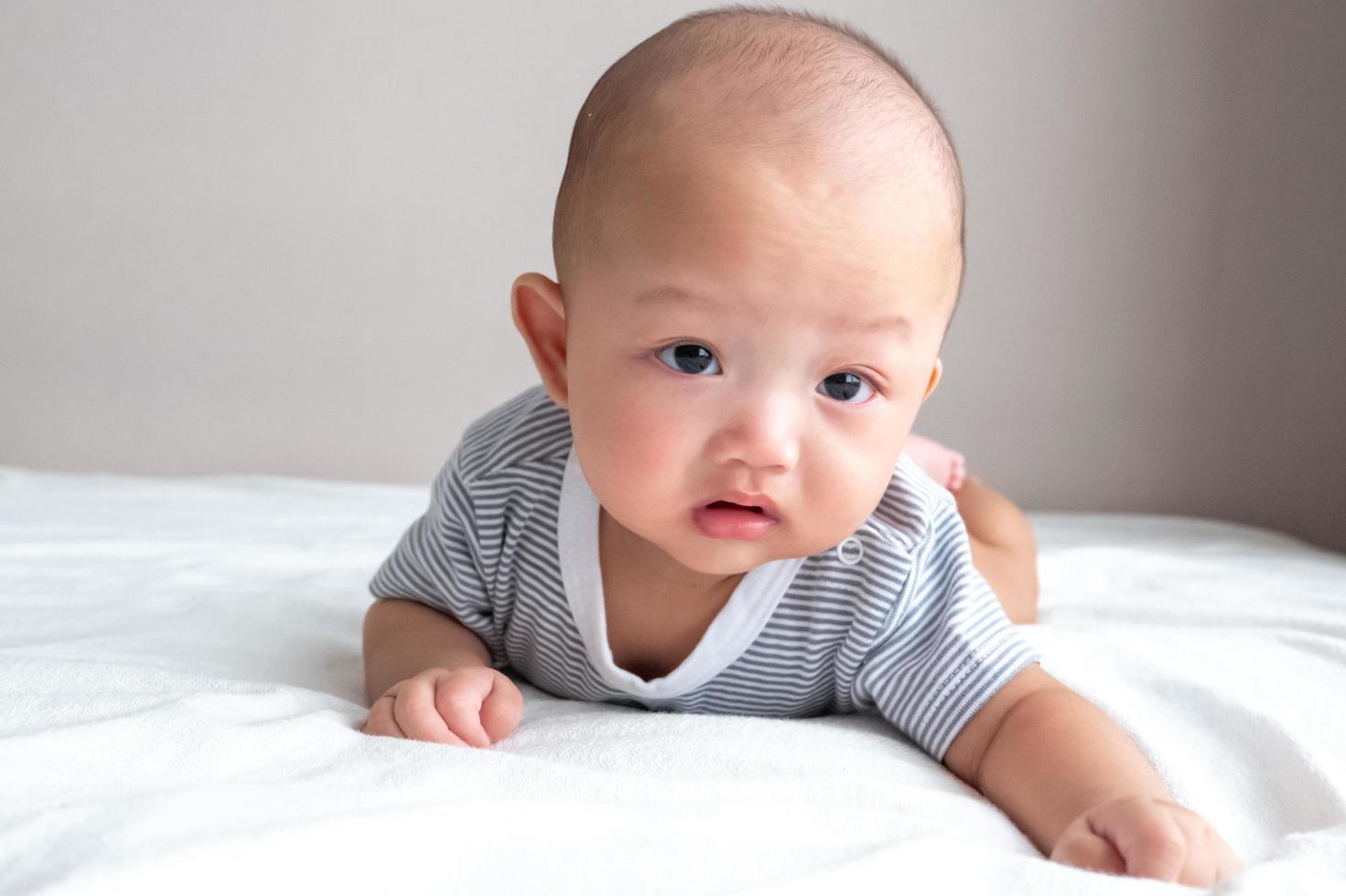 portrait Baby in a striped shirt, front view, crawling on a white mattress photo