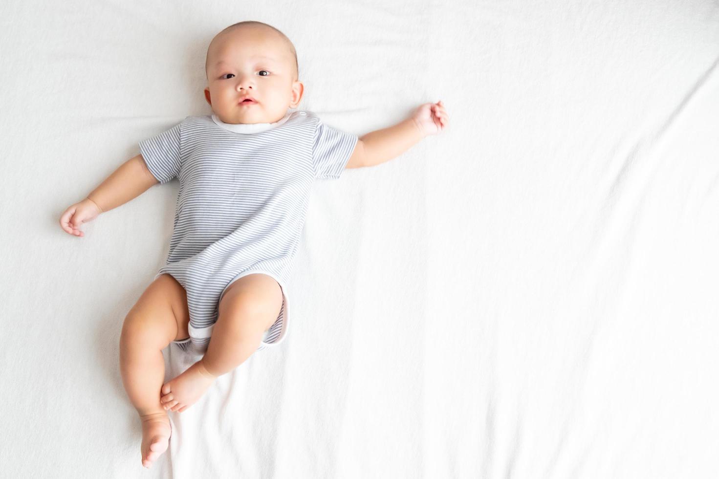 Top view and side area baby wearing a striped shirt, spreading arms and legs on a white carpet. photo