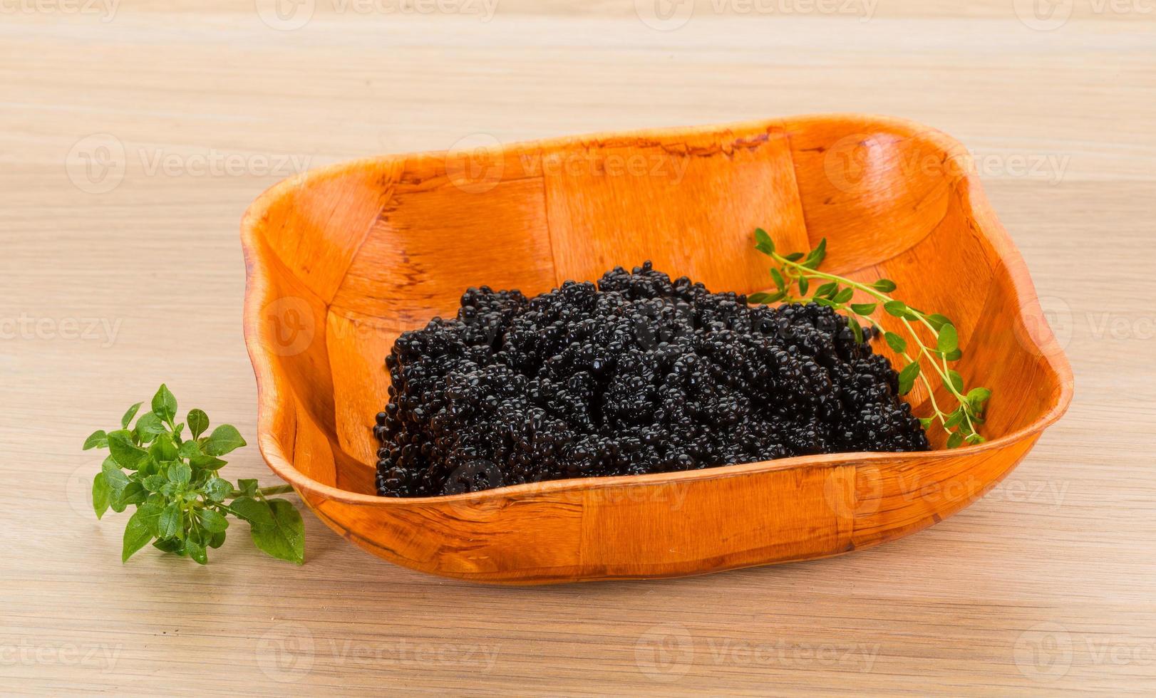 Black caviar in a bowl on wooden background photo