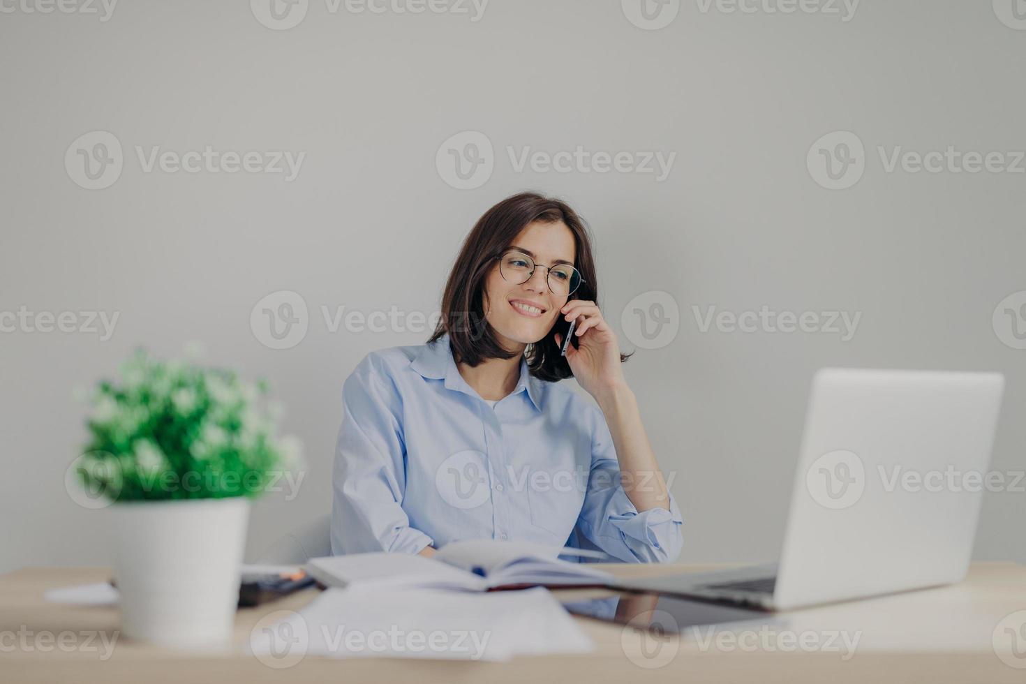 Beautiful female recruiter makes job offer to somene via cell phone, checks curriculum vitae on laptop computer, expalins detailes and pluses of work, surrounded with flower and personal diary photo