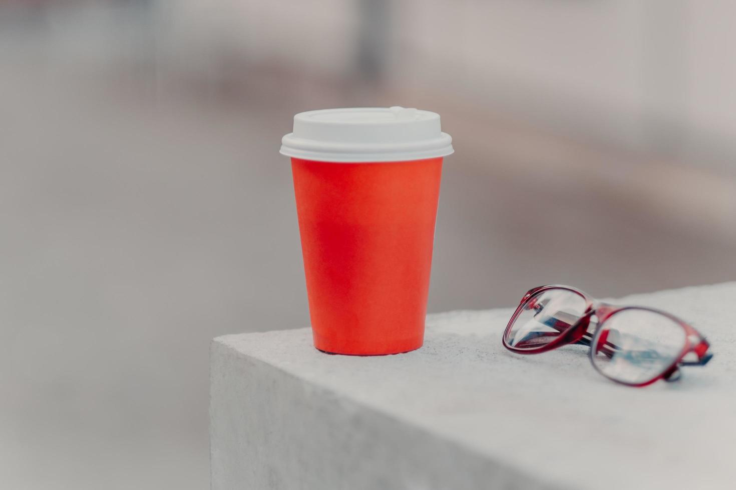 Horizontal shot of red coffee to go and optical glasses. Aromatic coffee for you to drink. Drinking concept. Paper cup of hot beverage photo