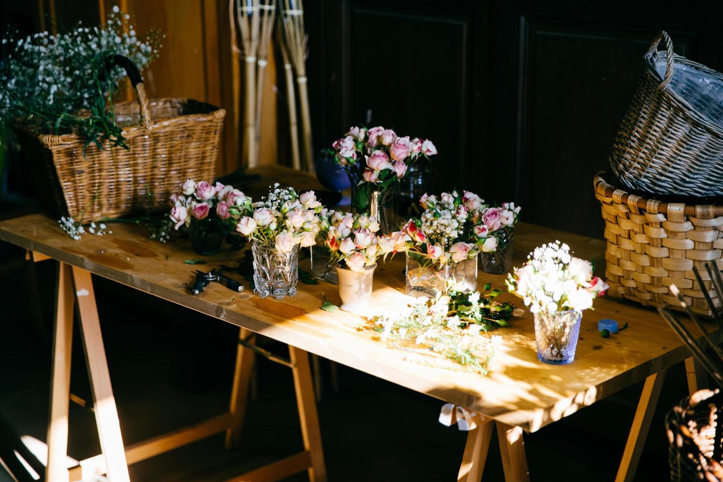 Long wooden table with different bouquetes of beautiful flowers. Pleasant smelling roses standing in glasses. Empty wooden backets. Creation of bunch of flowers. Roses arranged for decoration photo