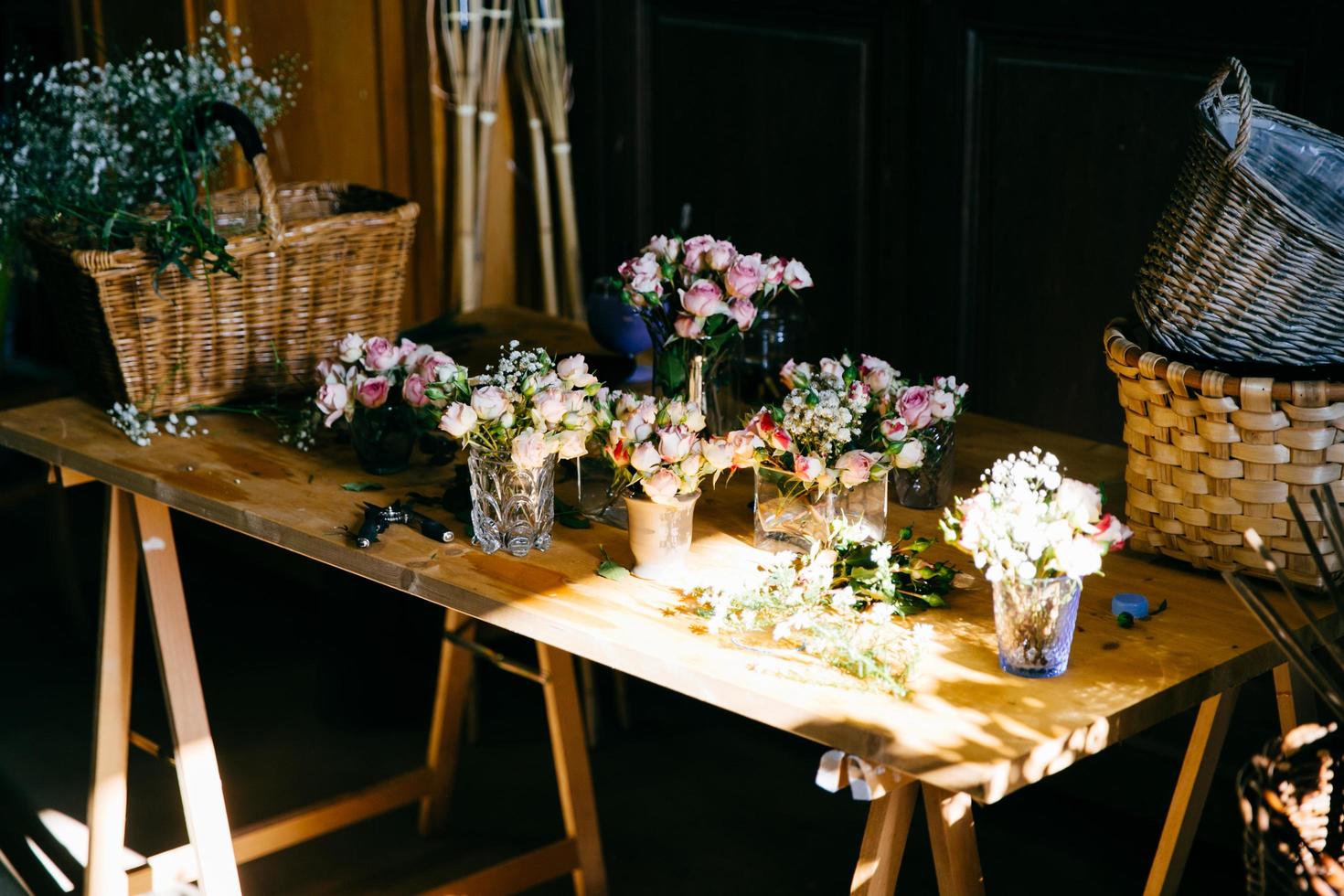 larga mesa de madera con diferentes ramos de hermosas flores. rosas de olor agradable de pie en vasos. respaldos de madera vacíos. creación de ramo de flores. rosas arregladas para decorar foto