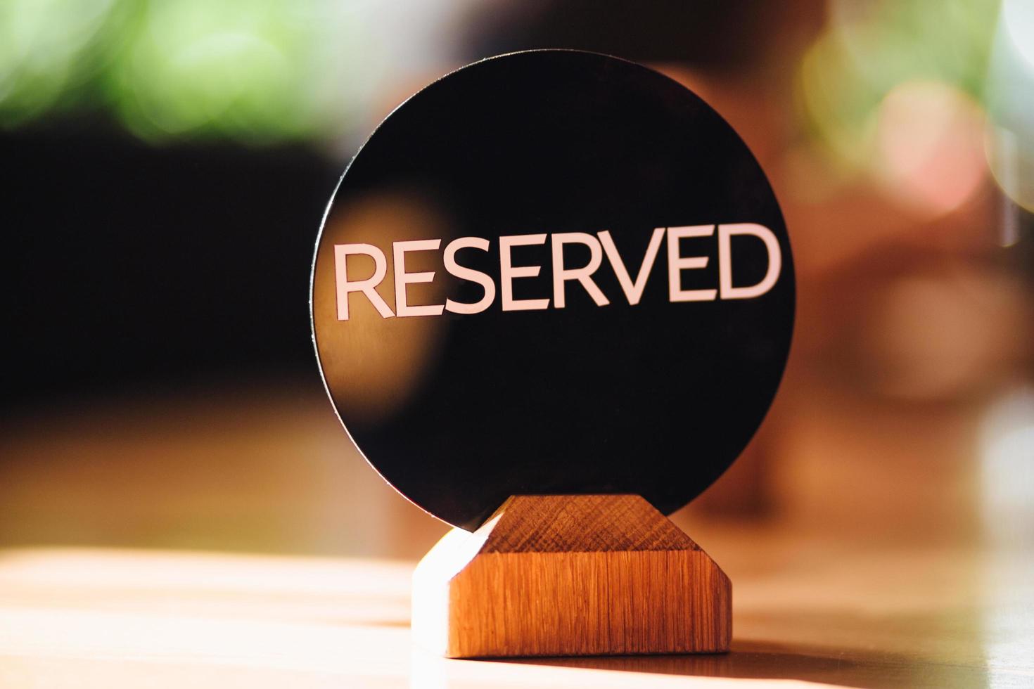 Indoor shot of reserved sig on wooden table in cafe, denotes that this place is occupied. Word reserved written in capital letters. Dont sit there, please photo