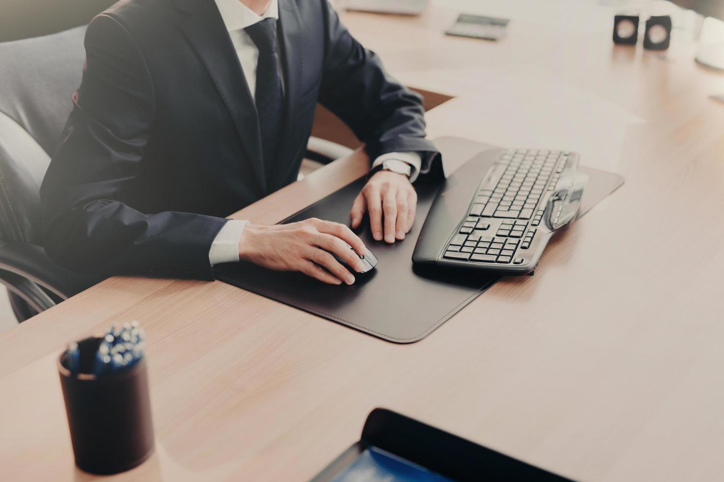 Cropped shot of elegant businessman works on computer in office, sits at work place, searches information in interent, keyboards something, being busy all day. People, working and business concept photo