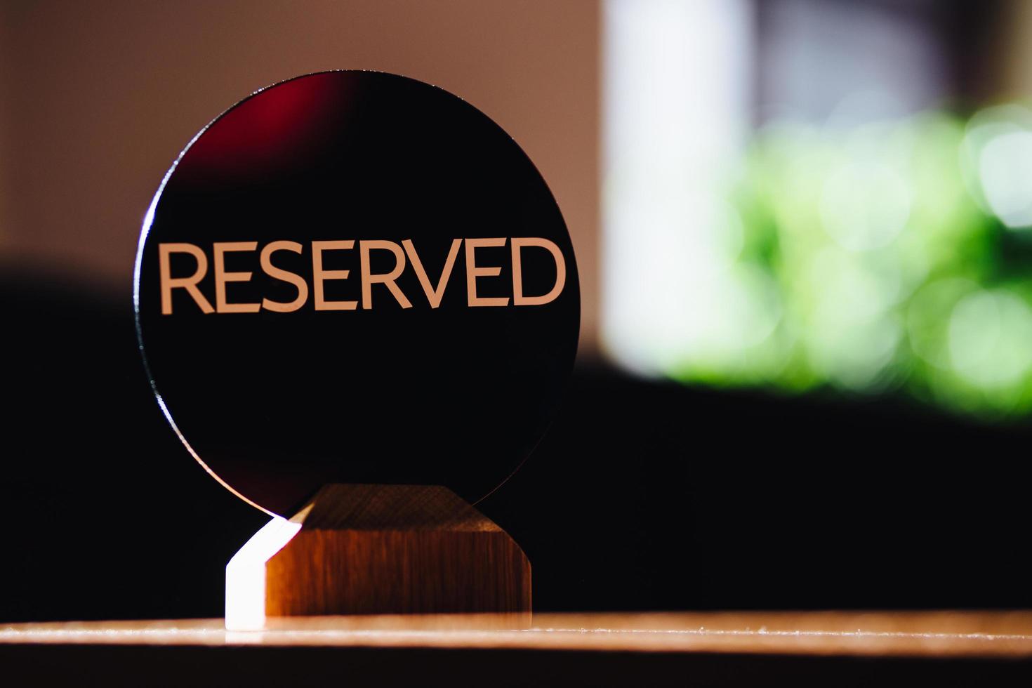 Table sign denoted reserved table in restaurant stands against blurred cafe background. Reservation concept. A tag of reservation. Beige on wooden table. photo