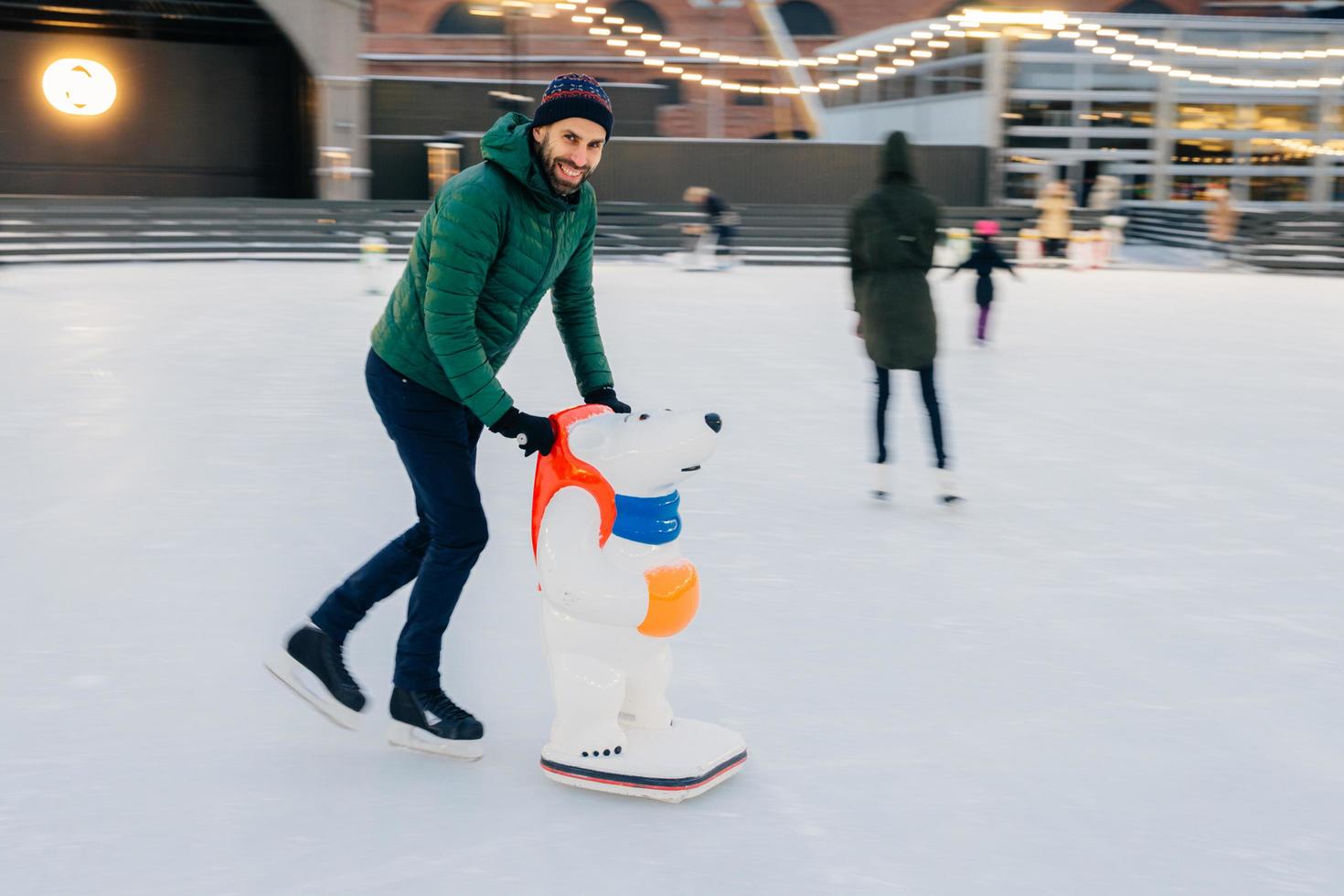 encantadores patines masculinos en la pista de patinaje con ayuda especial, prácticas para hacer algunos trucos, tiene una expresión feliz como si estuviera en el hielo por primera vez, se divierte con amigos. concepto de personas y ocio foto