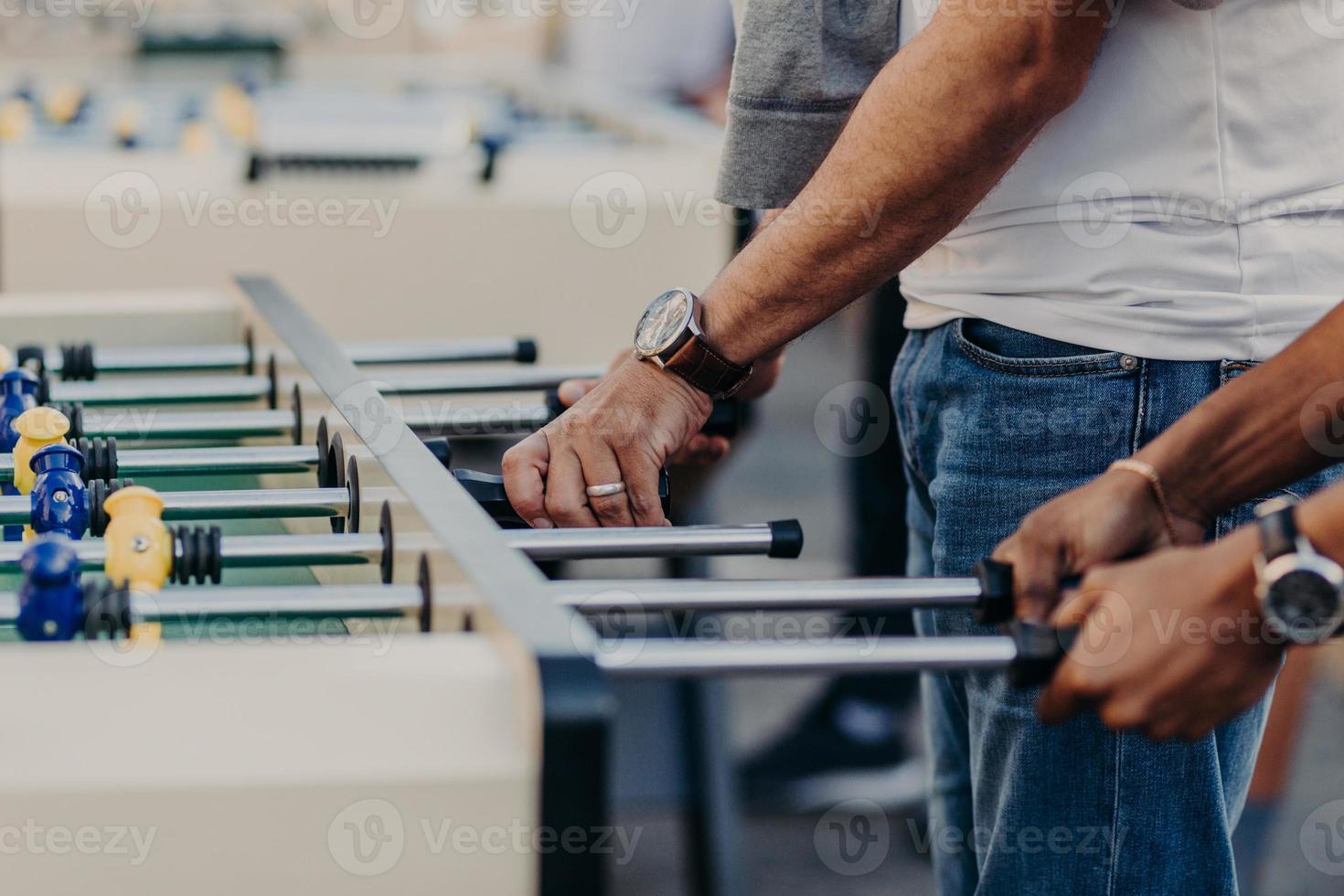 Group of active men play table football, have fun together, involved in games and entertainments. Guys play foosball. Gambling concept photo