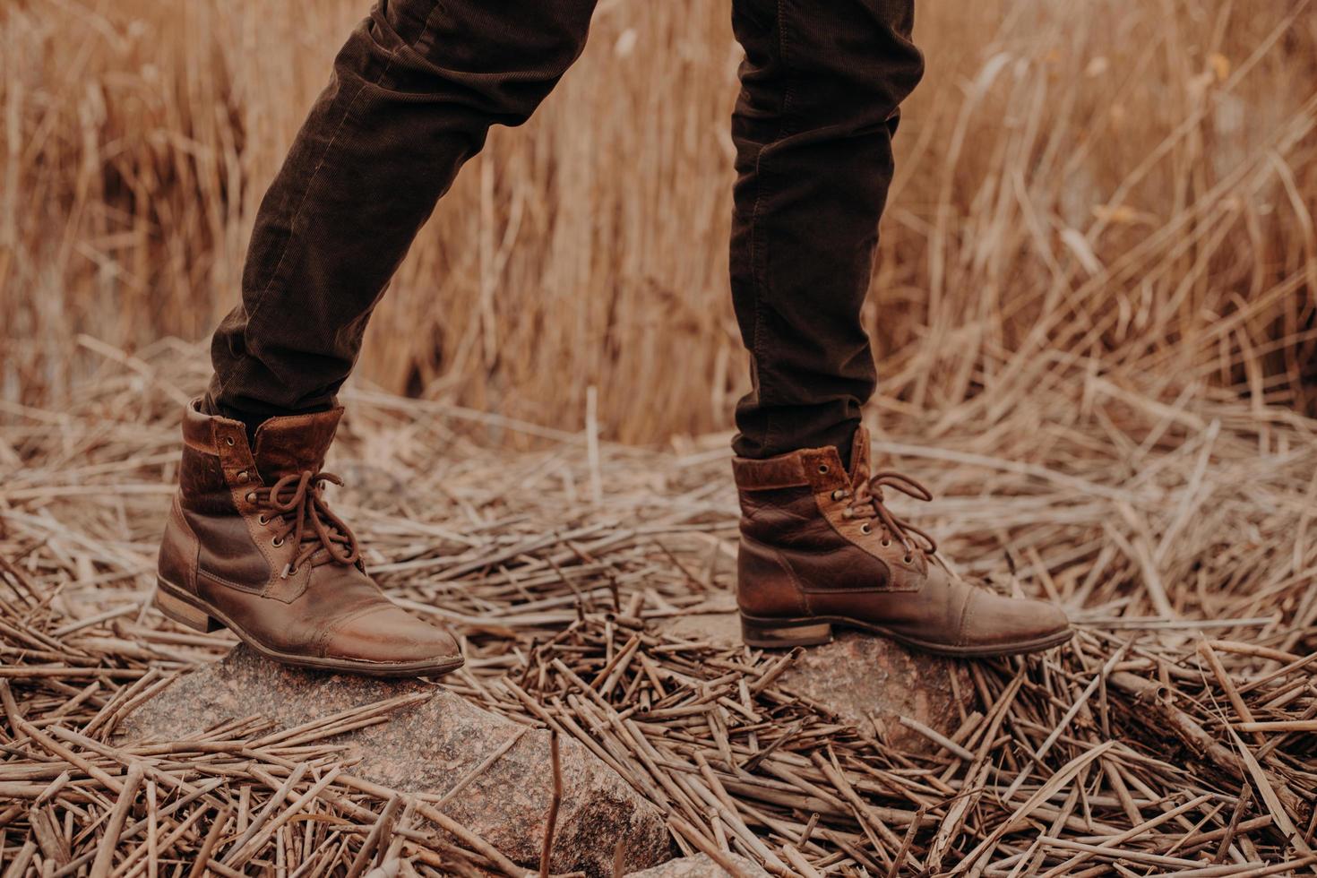 Cropped shot of unrecognizable man wears old leather brown footwear, poses on ground with stubble, walks at field alone. photo