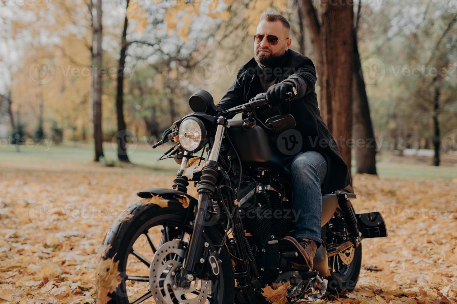 Male motorcyclist drives in nature on fast bike, wears shades, black jacket, gloves, jeans and boots, enjoys autumn season, spends free time actively, ready for long trip. People, transport, driving photo