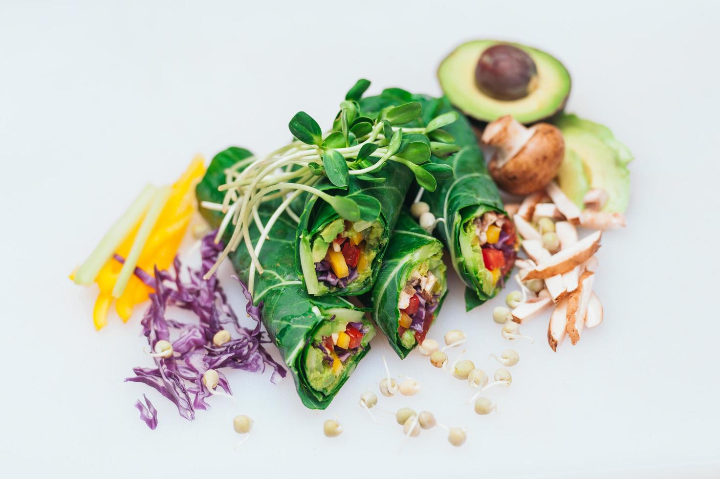 Vegan spring green rolls filled with pepper isolated over white background with avocado, mushrooms, purple cabbage. Peas sprouts on rolls. Collard greens photo