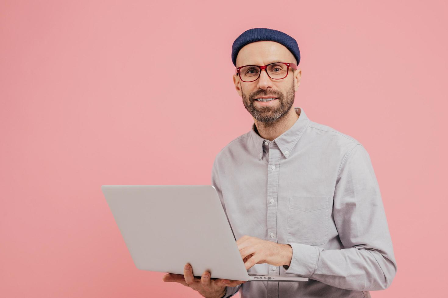 foto de un usuario de Internet que navega por el sitio web en una computadora portátil, conectado a Internet inalámbrico, sostiene un dispositivo electrónico, usa anteojos, pantalones formal, aislado sobre fondo rosa con espacio libre