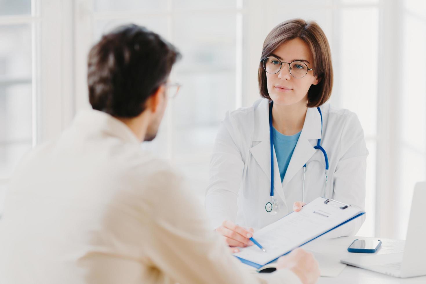 Female general practitioner explains which prescribed medicine patient should buy, gives medical visit consultation. Male clinic visitor tells about health complaints to therapist. Healthcare concept photo