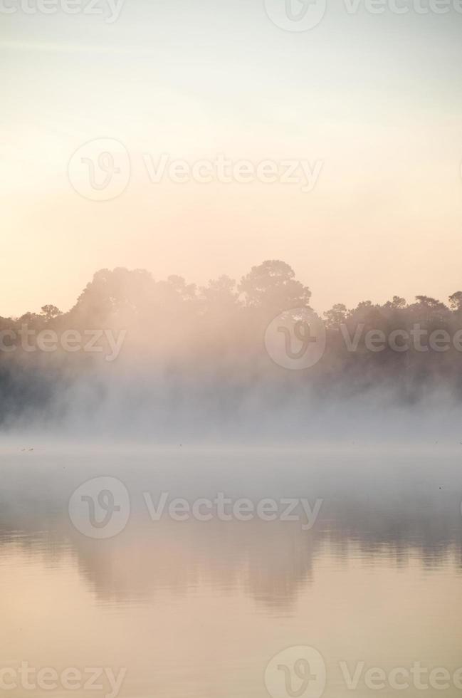 A mist drifts over the pond as the sun gradually lights the sky, the scene offering a moment of serenity and reflection. photo