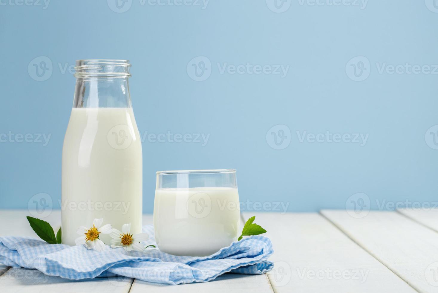 A bottle of milk and glass of milk on a white wooden table on a blue background, tasty, nutritious and healthy dairy products photo