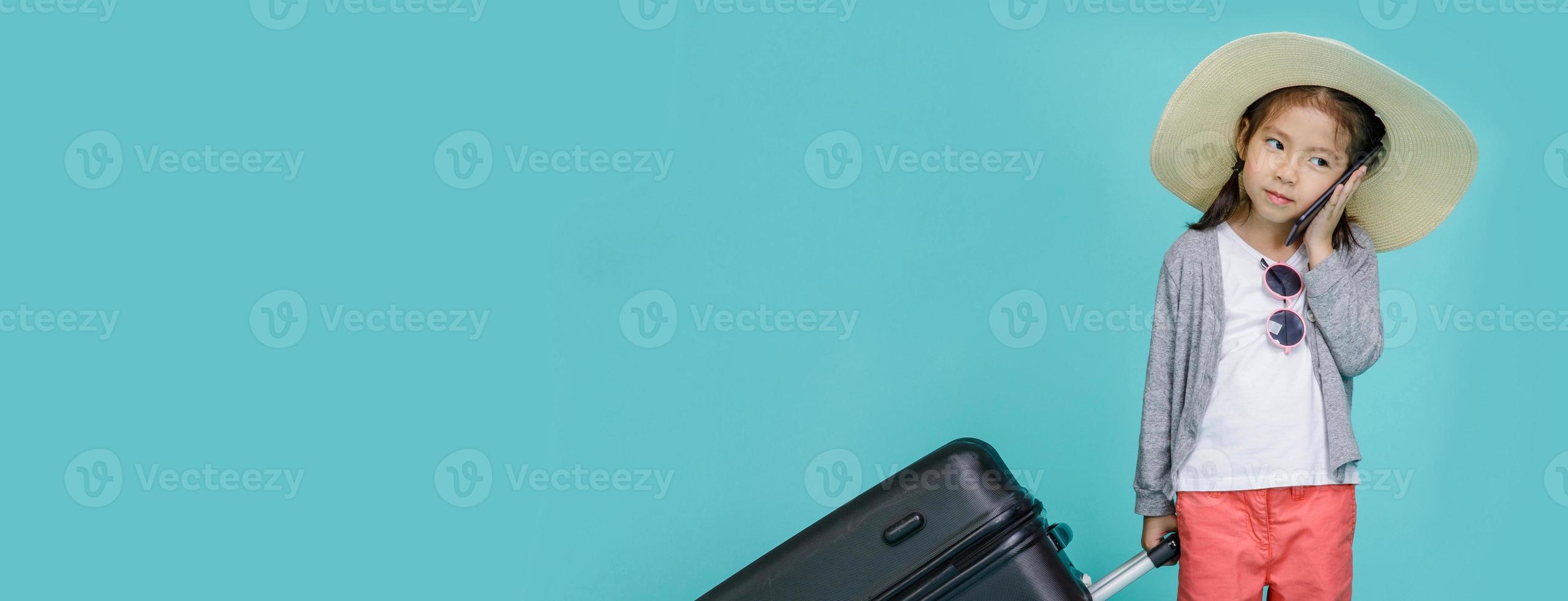 Asian little girl is using a smartphone to check flight to travel on weekends, empty space in studio shot isolated on colorful blue long banner background photo
