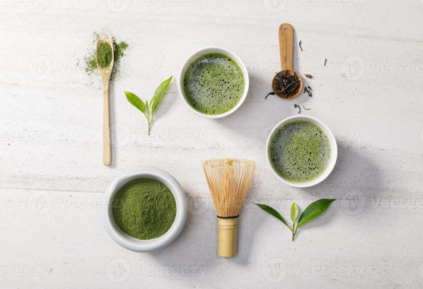 polvo de té verde matcha orgánico en un tazón con batidor de alambre y hoja de té verde sobre una mesa de piedra blanca, producto orgánico de la naturaleza para la salud con estilo tradicional foto