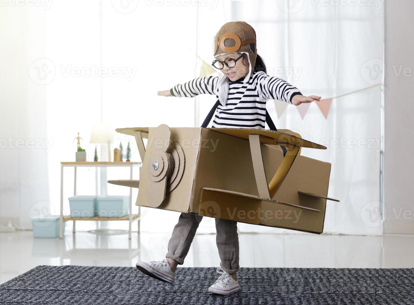 niña asiática jugando con artesanía de avión de juguete de cartón en la sala de estar con espacio de copia para su texto, creativa en casa y sueños de concepto de vuelo foto