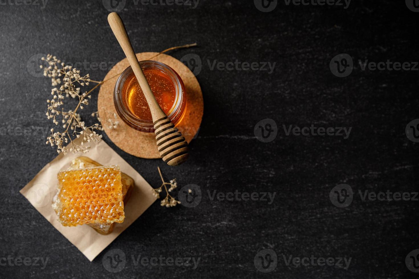 panal con cucharón de miel y flor seca sobre fondo negro, productos de abejas por concepto de ingredientes naturales orgánicos foto