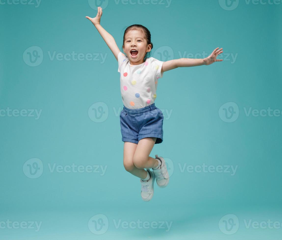 Playful energetic Asian little girl jumping in mid-air, empty space in studio shot isolated on colorful blue background photo