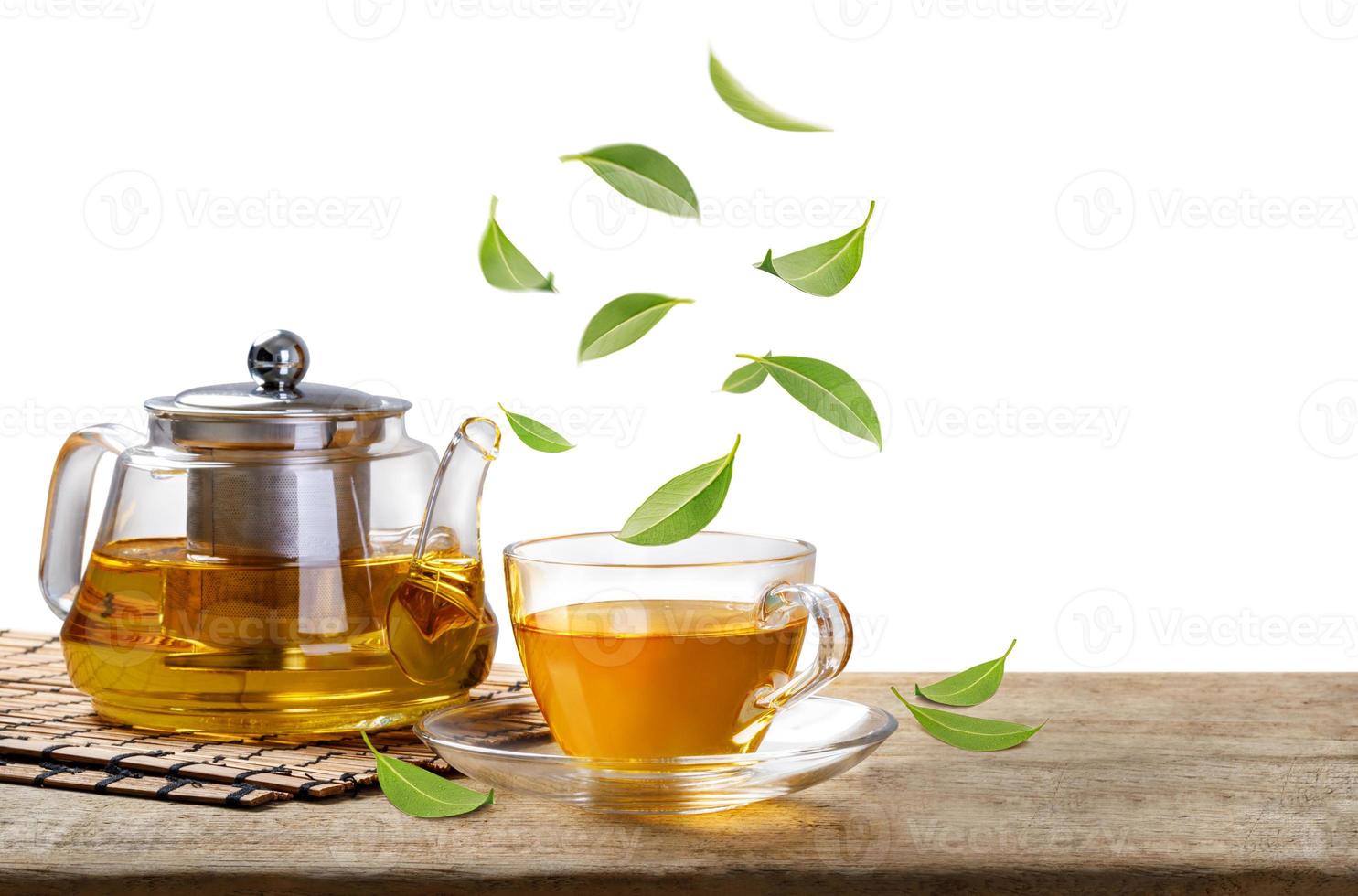 Jug and hot tea glass cup with flying whirl green tea leaves in the air, Healthy products by organic natural ingredients concept, Empty space in studio shot isolated on white background photo