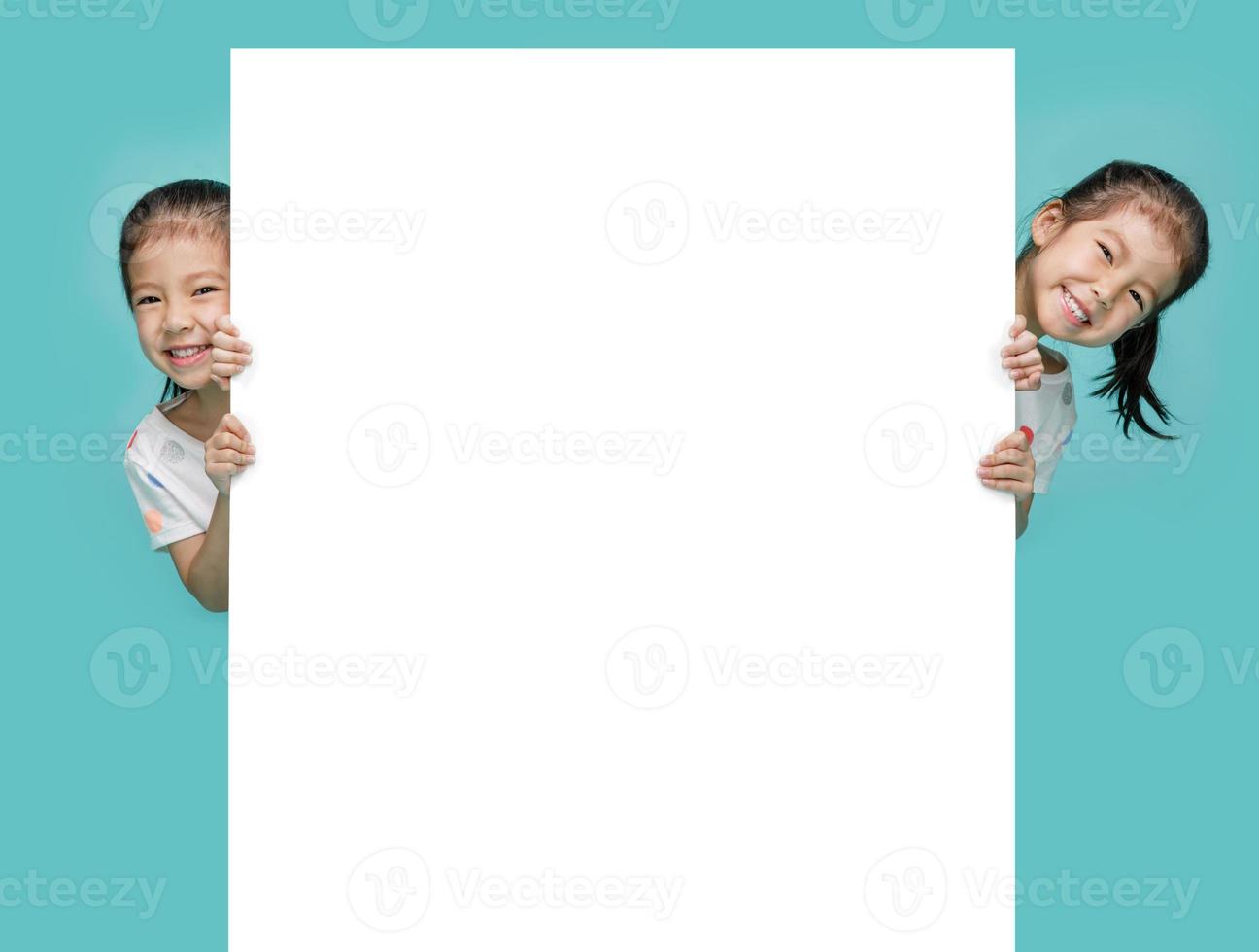 niñas asiáticas emocionadas escondidas detrás de una pizarra en blanco, espacio vacío en una foto de estudio aislada en un fondo azul colorido