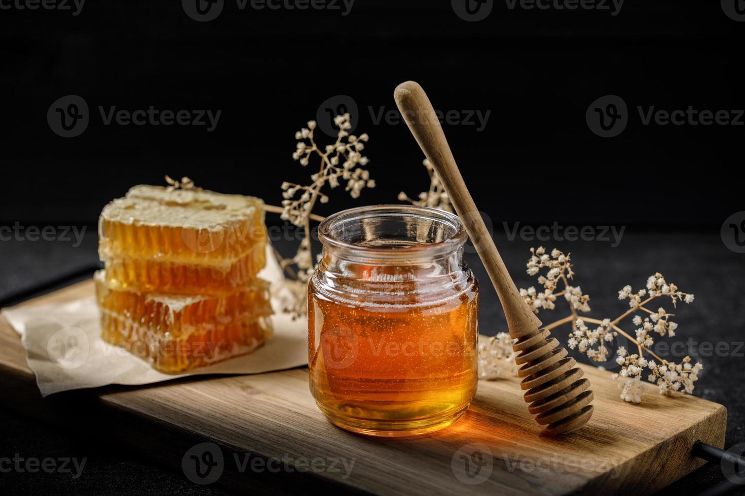 panal con cucharón de miel y flor seca sobre fondo negro, productos de abejas por concepto de ingredientes naturales orgánicos foto