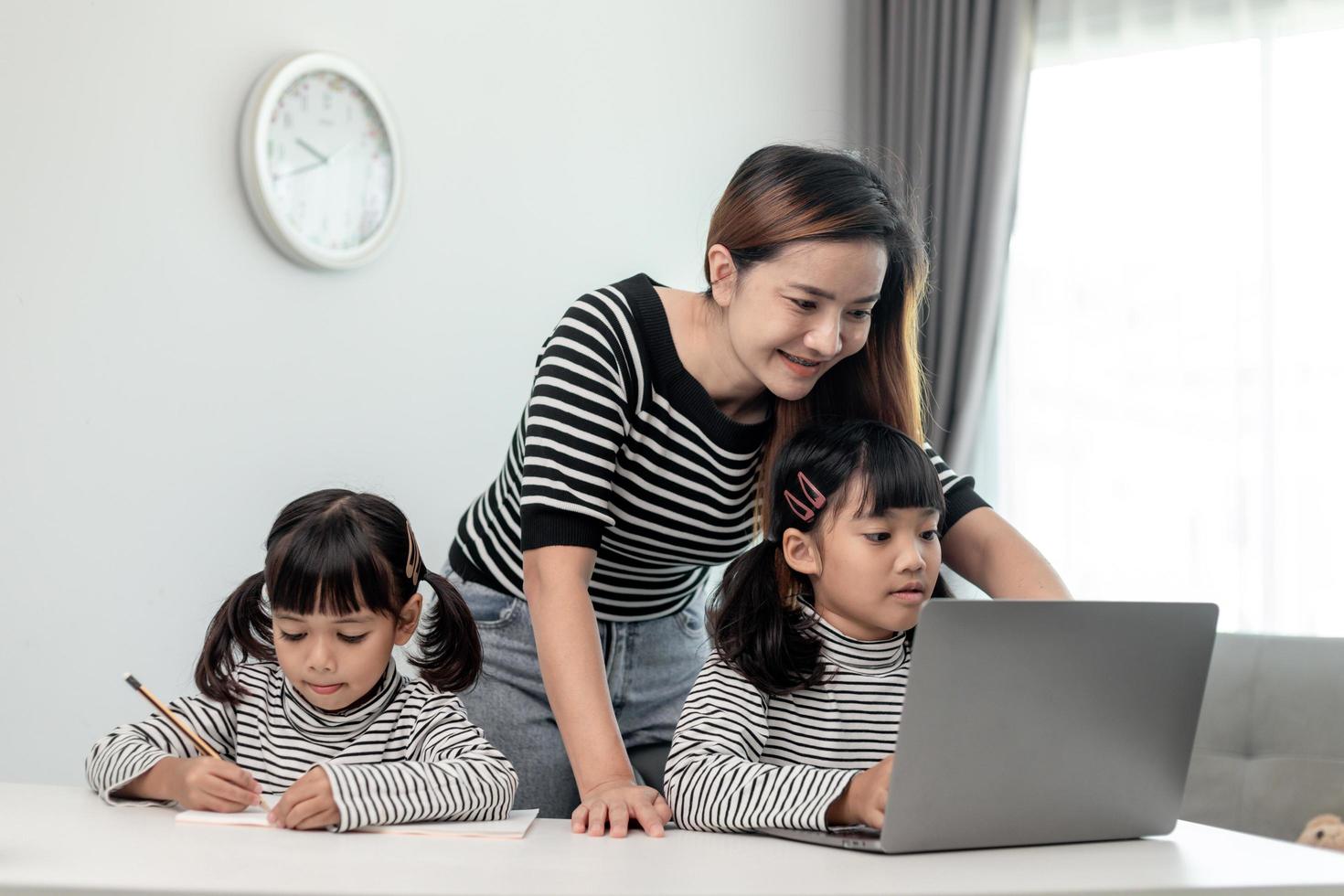 Asian little young girl kid learning online class at home with mother. Preschool child use laptop computer do homework, homeschool from school teacher by digital remote internet with support from mom. photo