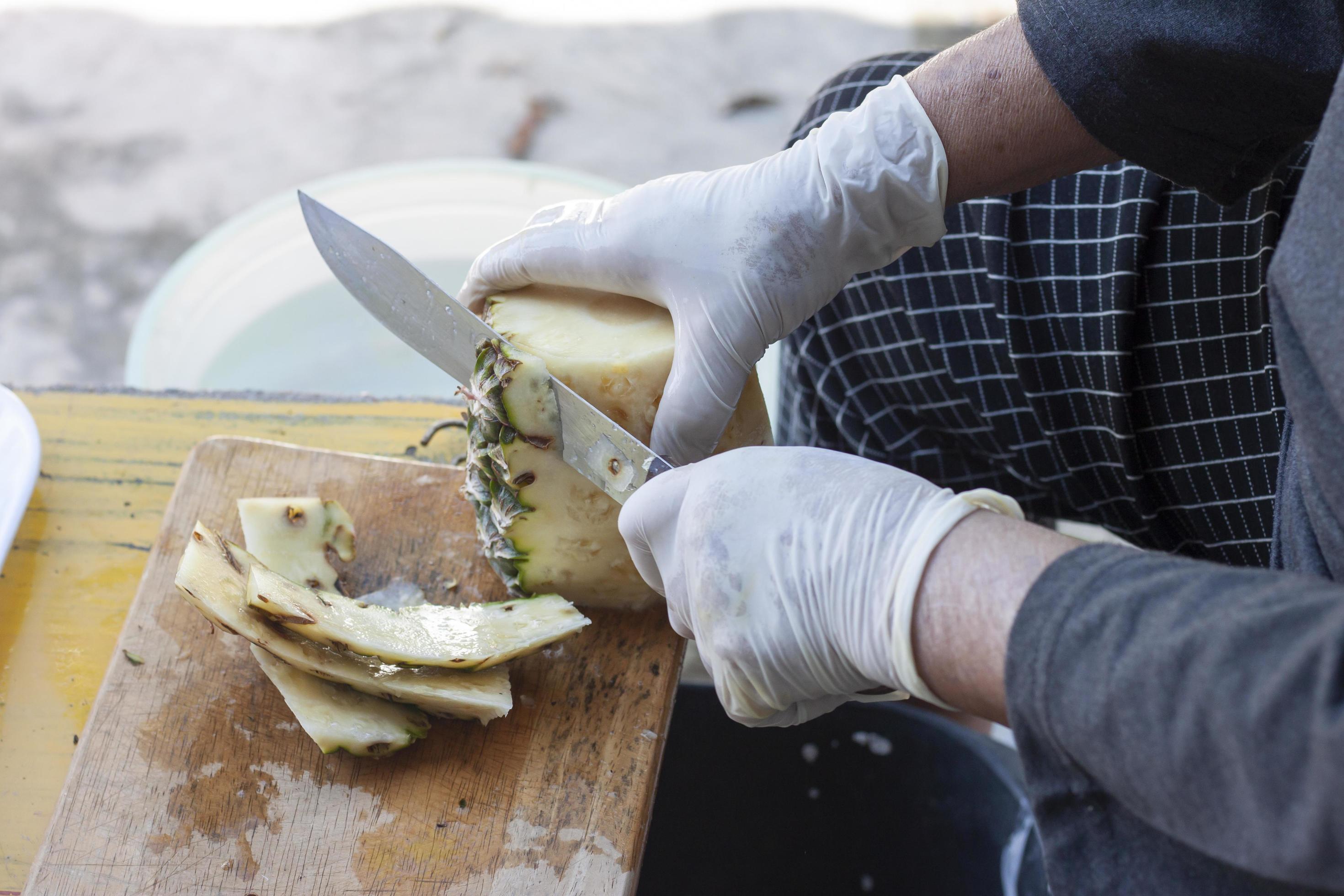 Hand of street vendor holding knife peeling pineapples for sale to