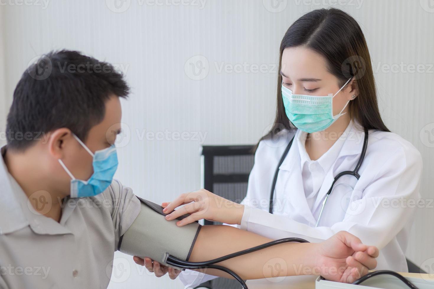 Asian woman doctor uses a blood pressure meter with a man patient photo