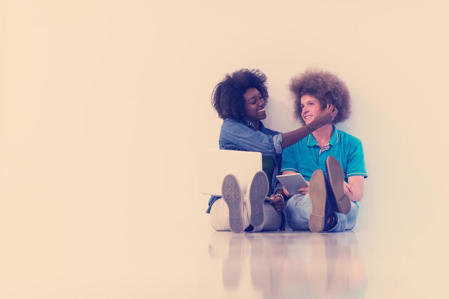 multiethnic couple sitting on the floor with a laptop and tablet photo