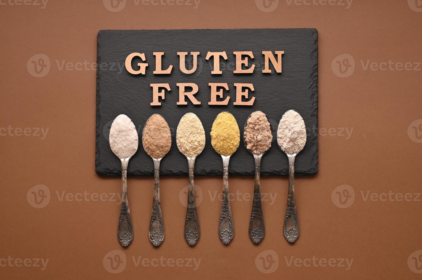 Gluten free text and spoons of various gluten free flour, almond, buckwheat, rice, corn, oat, chickpea. Flat lay, top photo