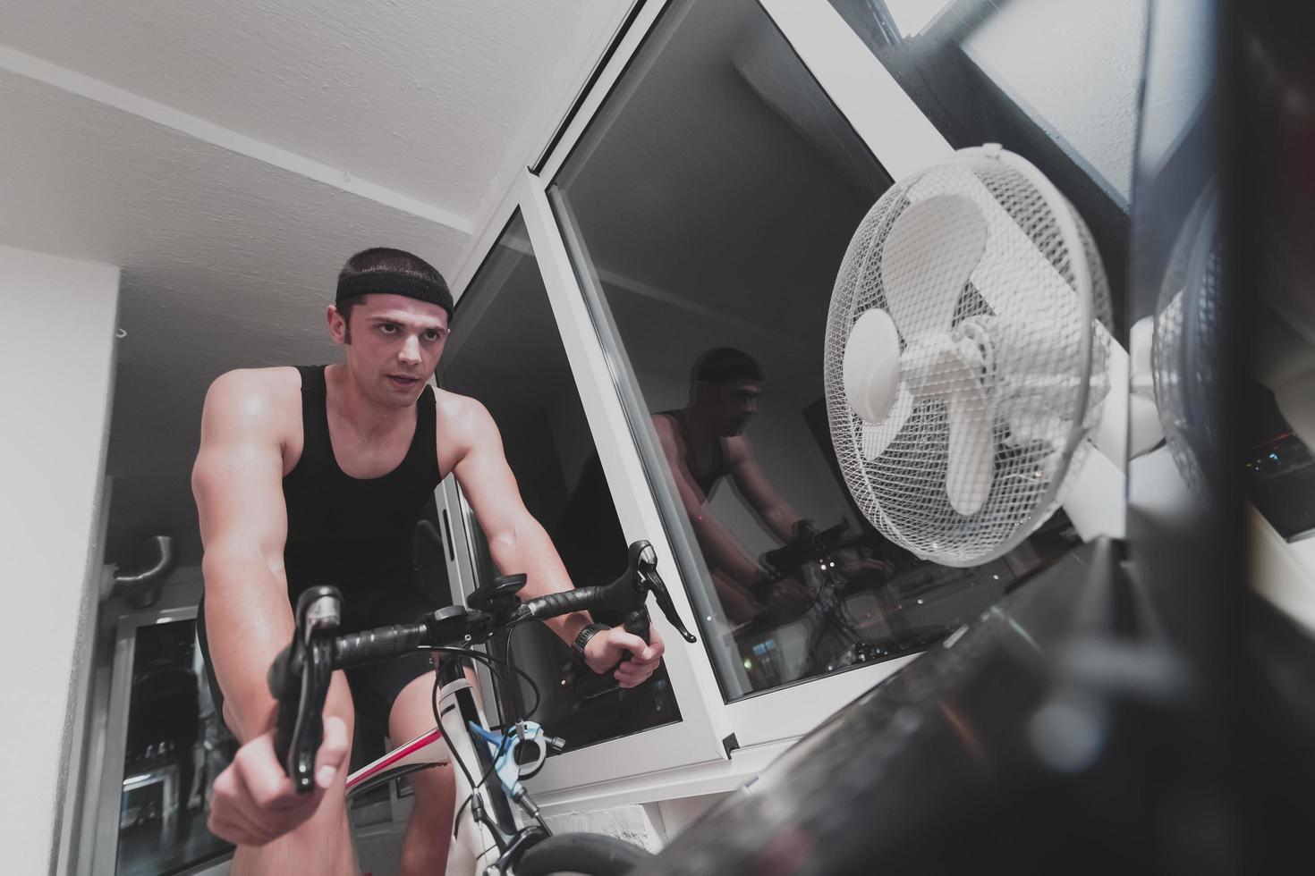 Man cycling on the machine trainer he is exercising in the home at night playing online bike racing game photo