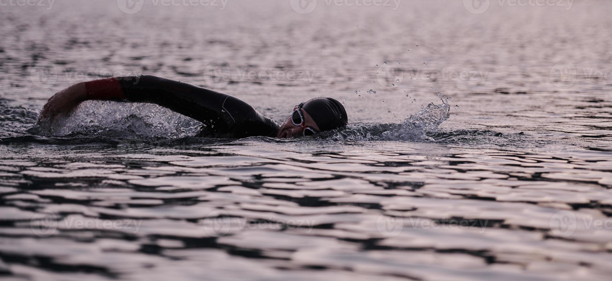 atleta de triatlón nadando en el lago al amanecer usando traje de neopreno foto